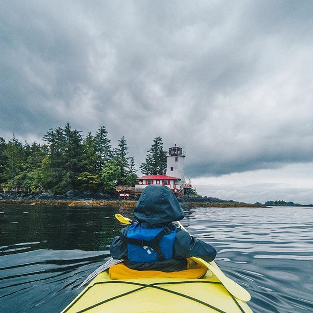 Photo of child kayaking in yellow kayak with a white lighthouse with red roof on the island in front of him.