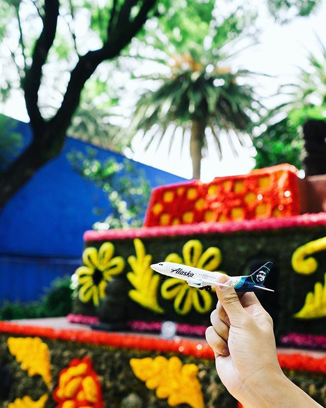 This is a photo of a bright colored museum display with a person holding up a mini Alaska Airlines plane in front of it