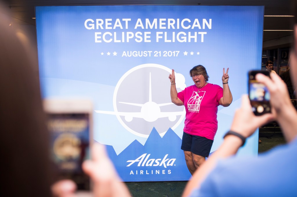 Kimberly Cassia stands in front of the Great American Eclipse Flight poster at the gate while onlookers snap photos.