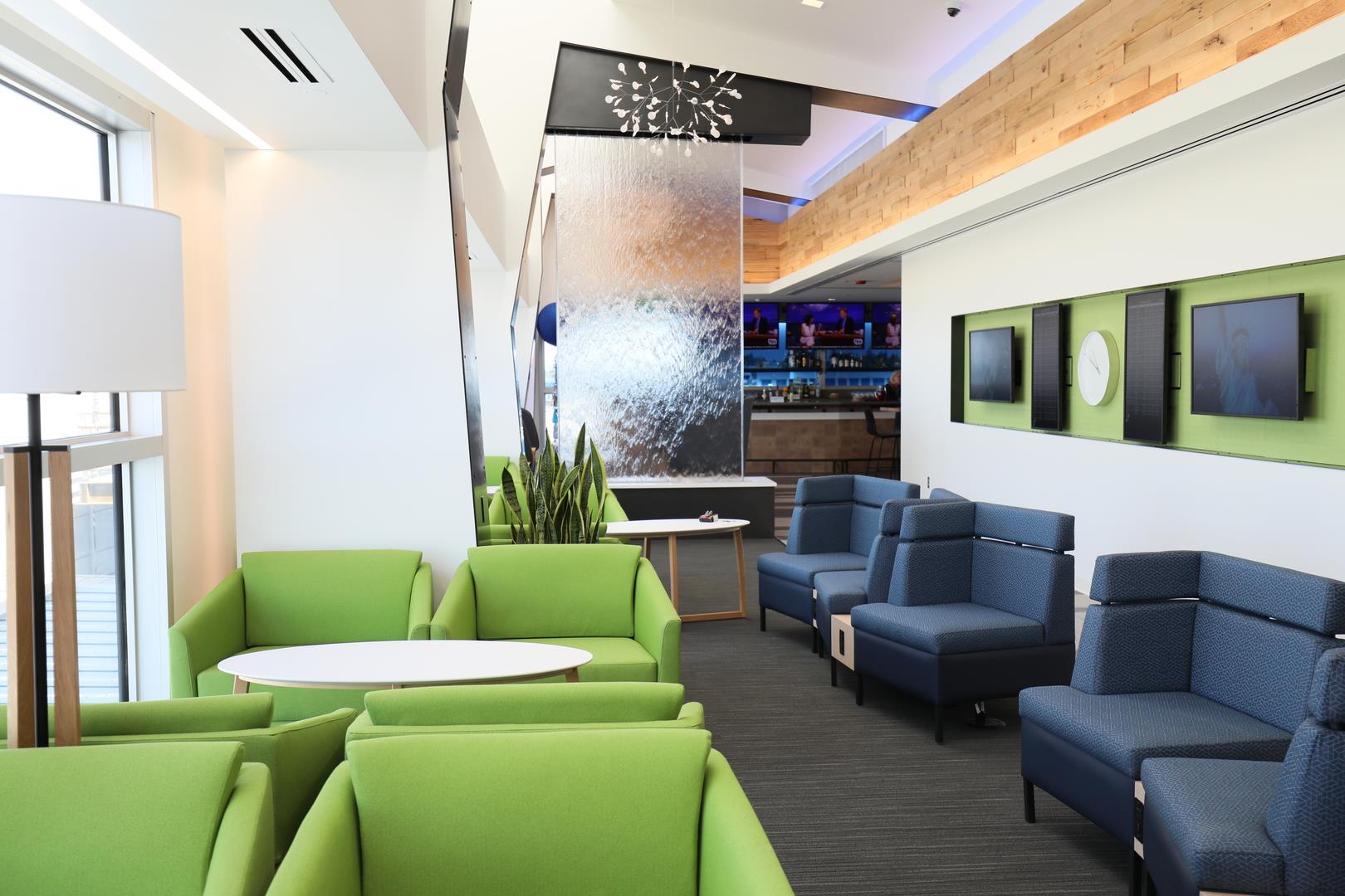 This is a photo of the new Alaska Lounge with green and navy seats, flatscreen TVs and a glass wall.