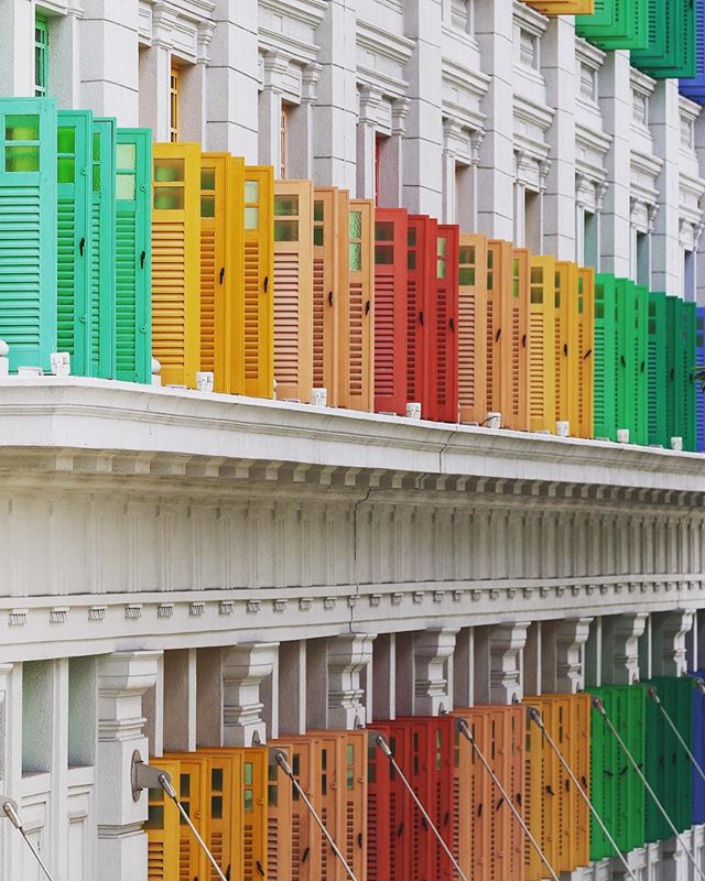 This is a photo of a white colonial style building with all of the shutters painted in greens, oranges, reds, yellows and blues.