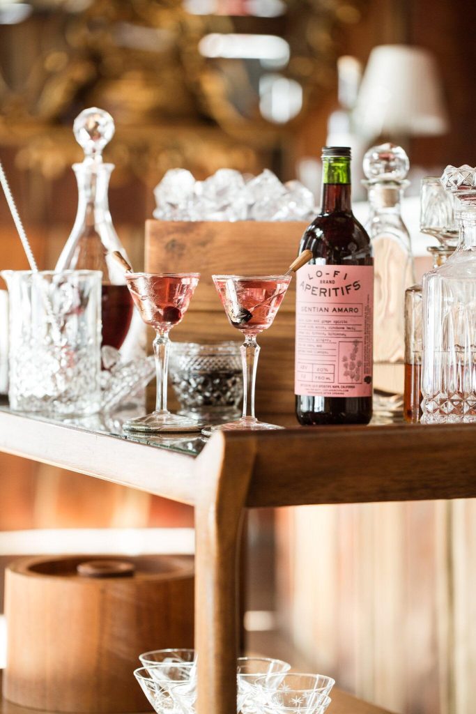 This is a photo of a bar cart with a bottle of liquor, mixers and a glass.