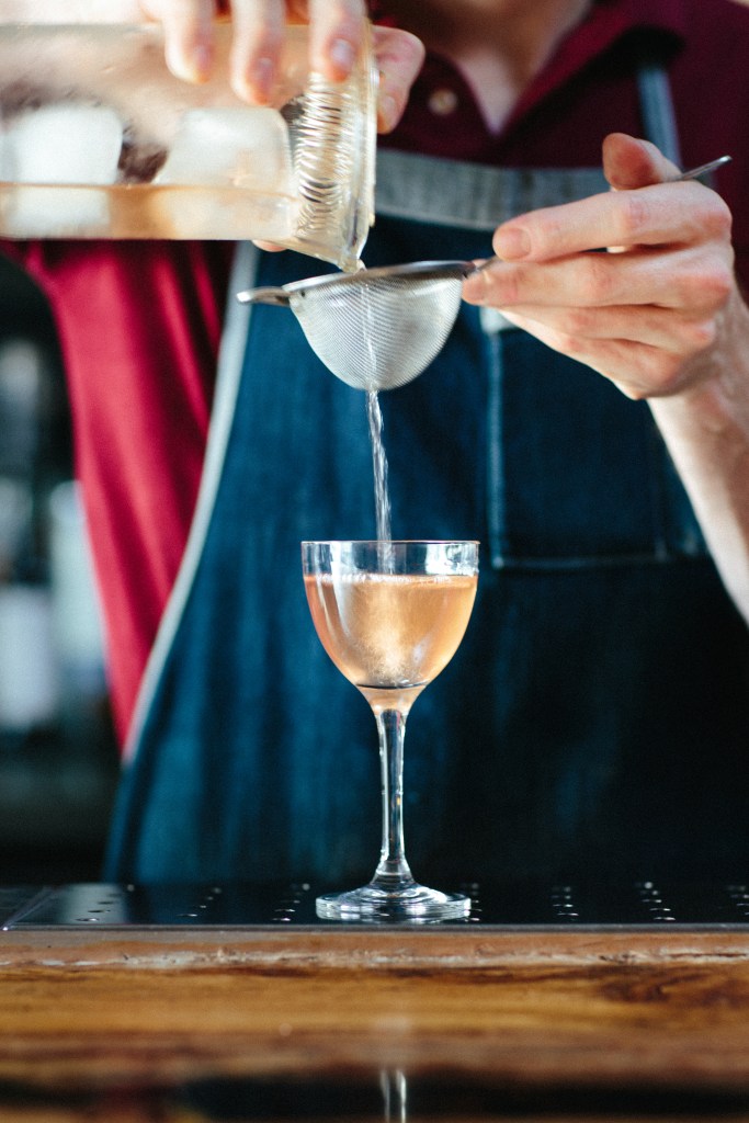 This is a photo of a bartender straining a mixed drink through a strainer into a glass