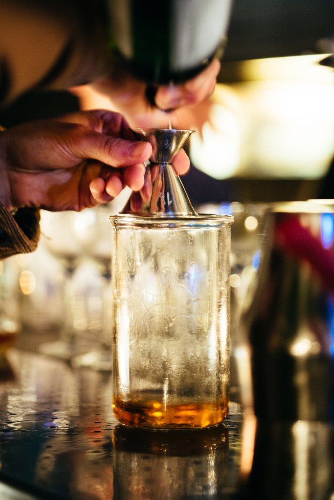 This is a photo of someone pouring a brown liquor into a glass through a strainer.