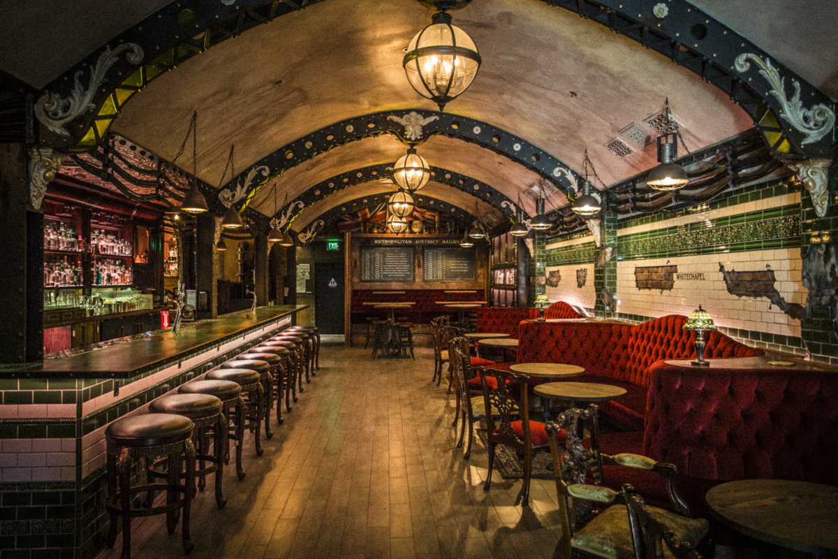 This is a photo of the Whitechapel Bar. It features wooden floors, a bar on the left with tiling and red sofas on the right. The ceiling is dome-shaped.