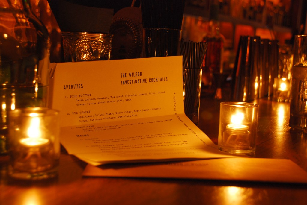 This is a photo of the paper menu sitting folded on top of the bar. The bar is dark and lit with candles.