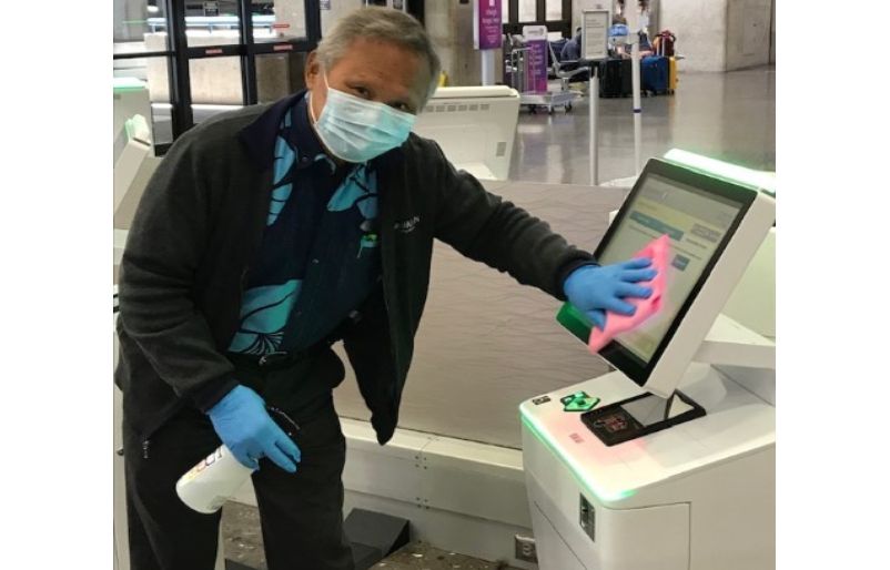 Guest Service Agent Avelino Sabog smiles at the camera behind his mask as he sanitizes a check-in kiosk at HNL. HNL