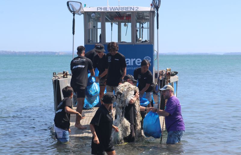 Team Kōkua and Sea Cleaners volunteers working together to load a boat with bags of collected debris. IMG_0948